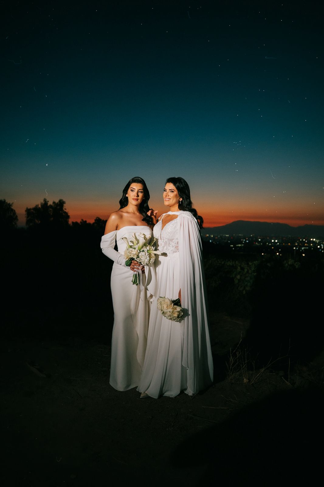 Dos novias con ramos blancos al atardecer bajo un cielo estrellado