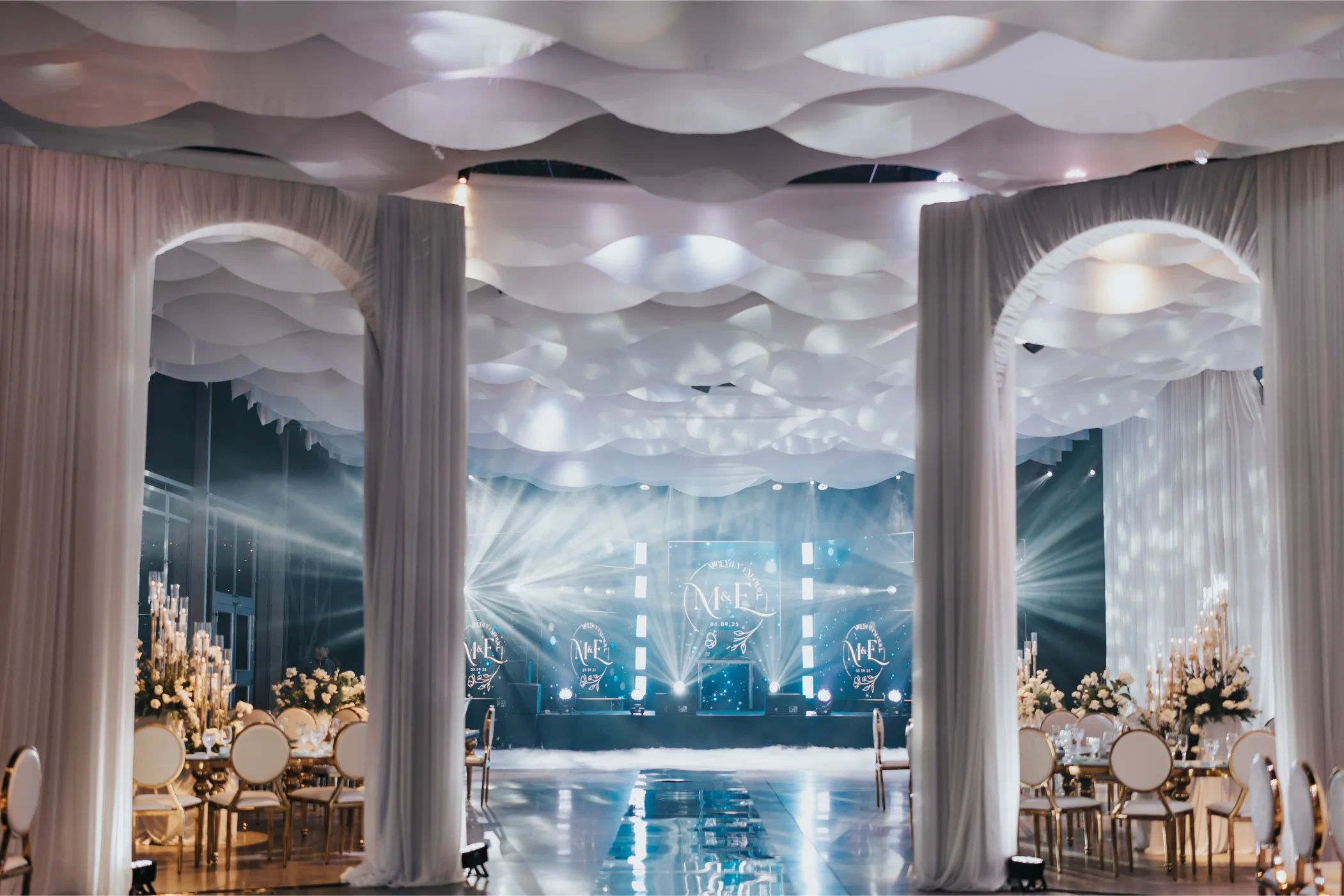 Boda Exequiel y Mireya, salón con cielo de telas onduladas, arcos y escenario iluminado con monograma M&E