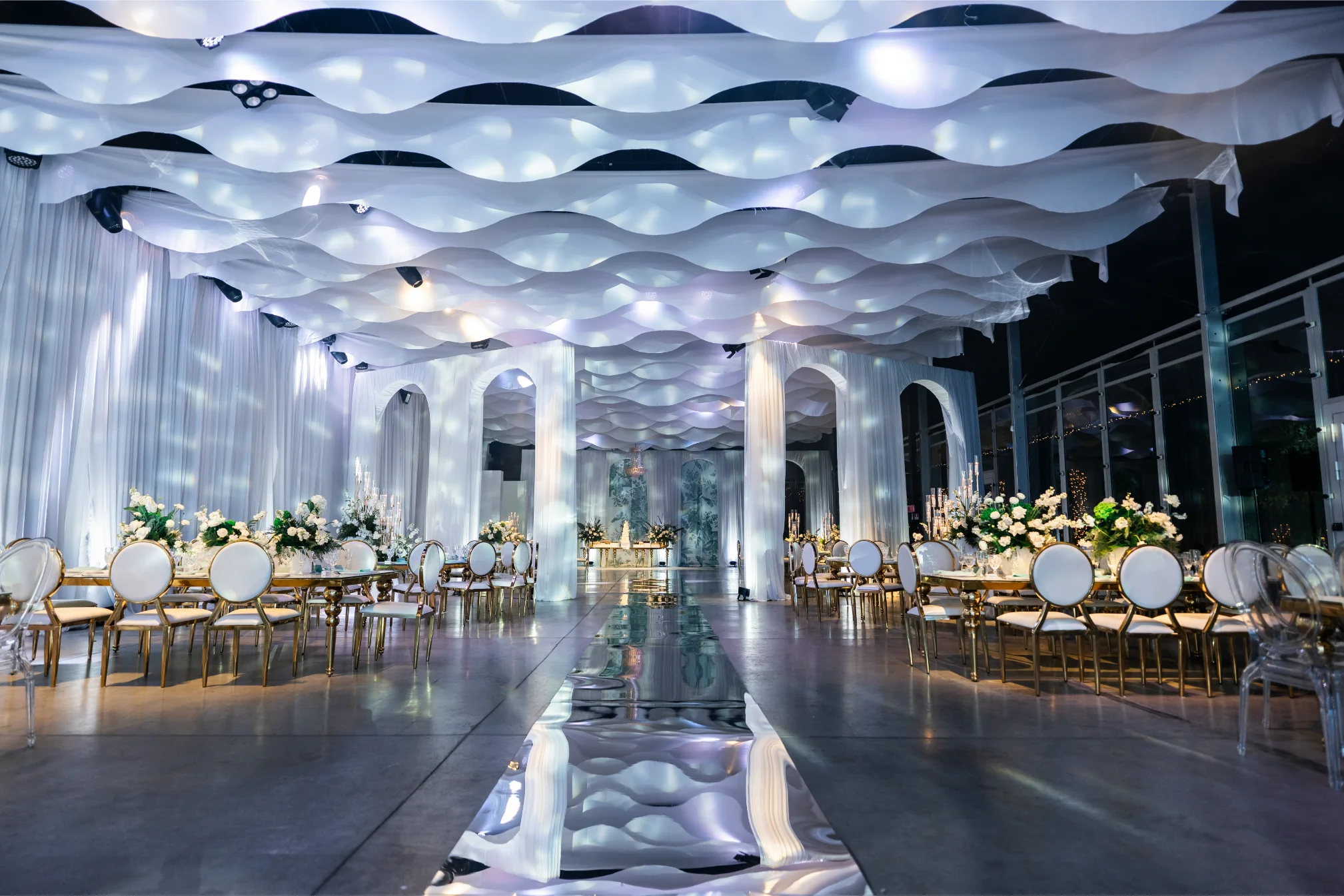 Boda Exequiel y Mireya, salón panorámico con mesas doradas, arreglos blancos y pasarela de espejo