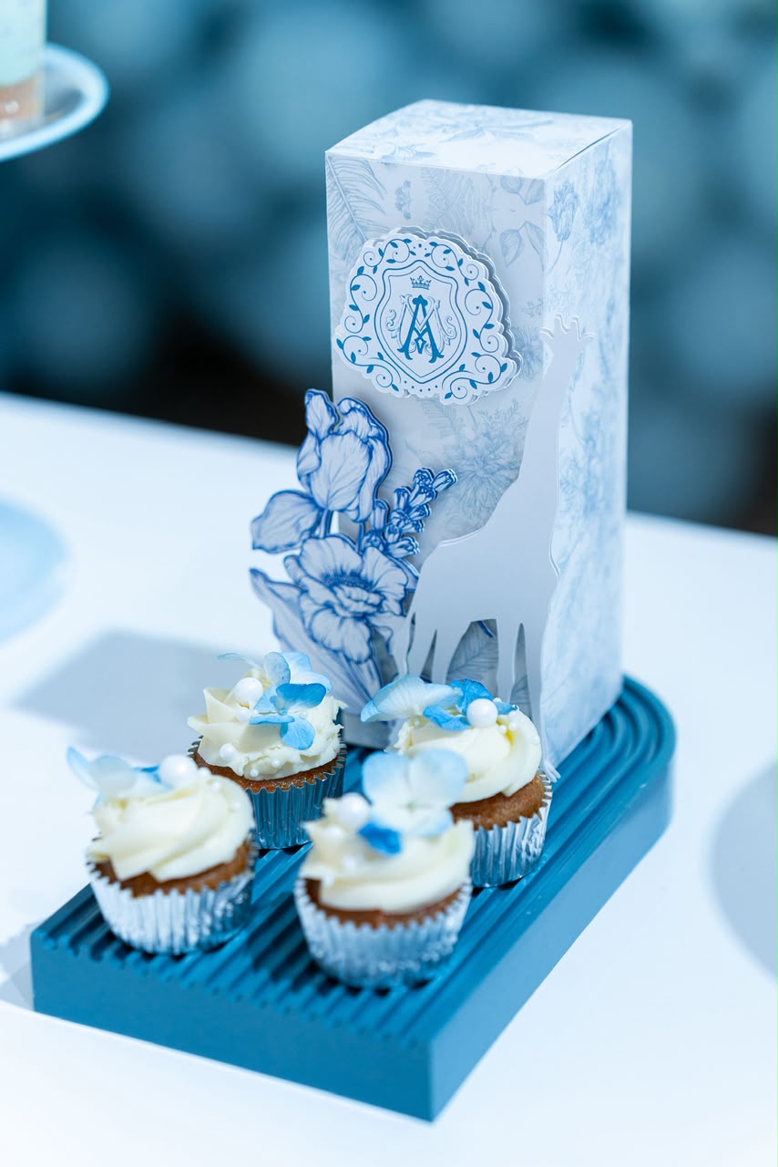 Cupcakes con hortensias azules junto a caja decorada con motivo toile y monograma