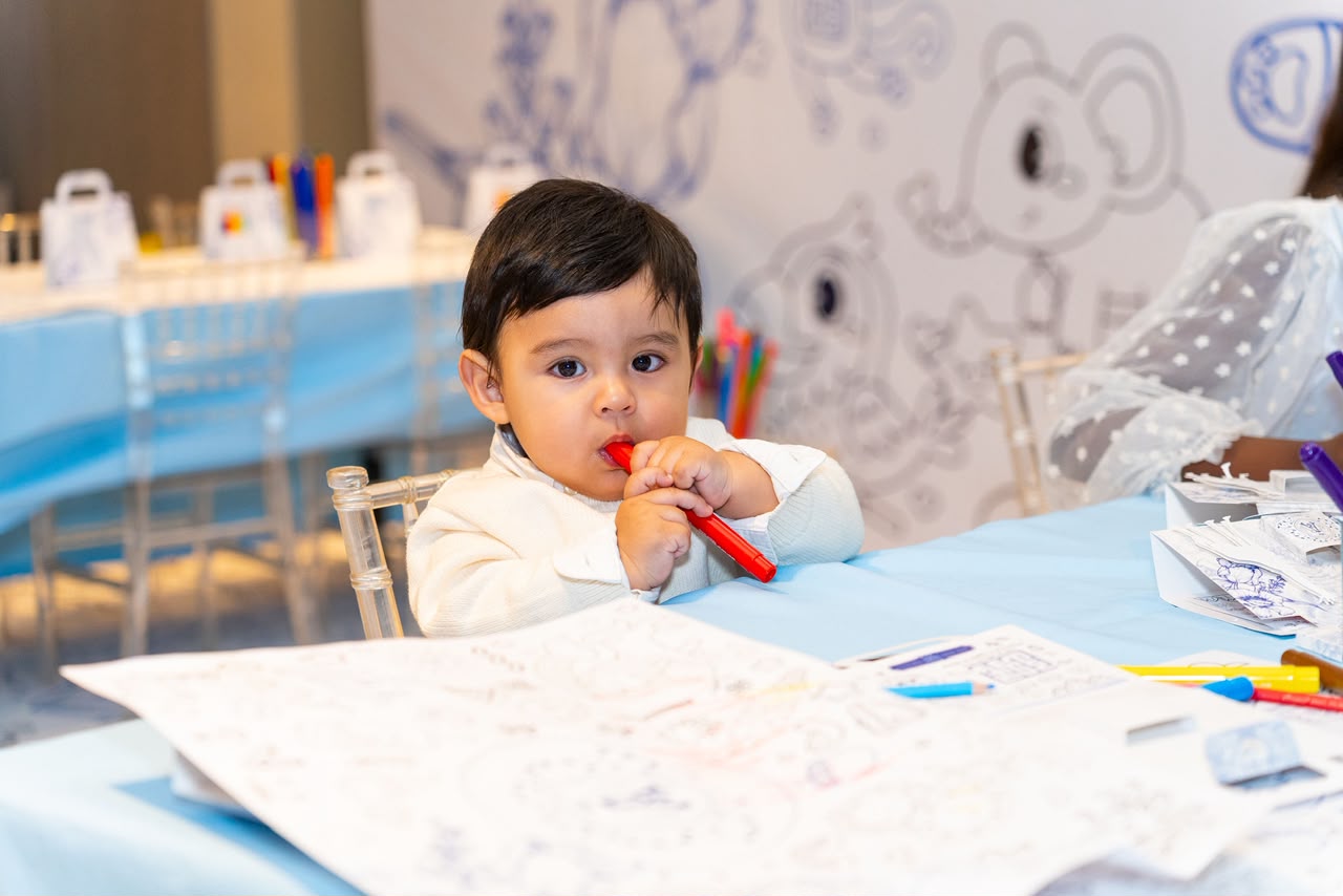 Bebé coloreando en la zona de niños con mantel azul y mural ilustrado