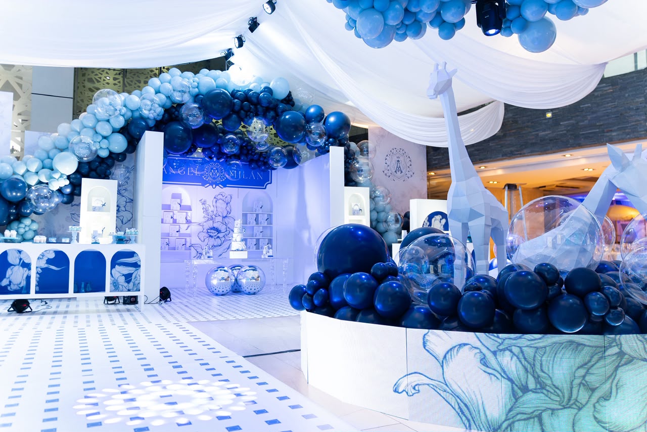Bautizo Ángel Milán, ambientación en tonos azules con arco de globos, jirafas de papel y esferas espejadas
